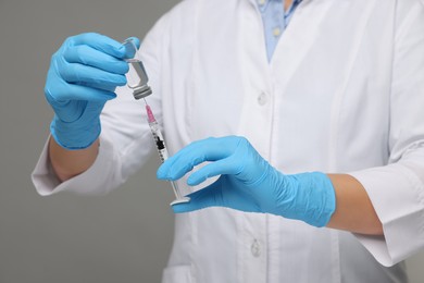 Doctor filling syringe with medication from glass vial on grey background, closeup