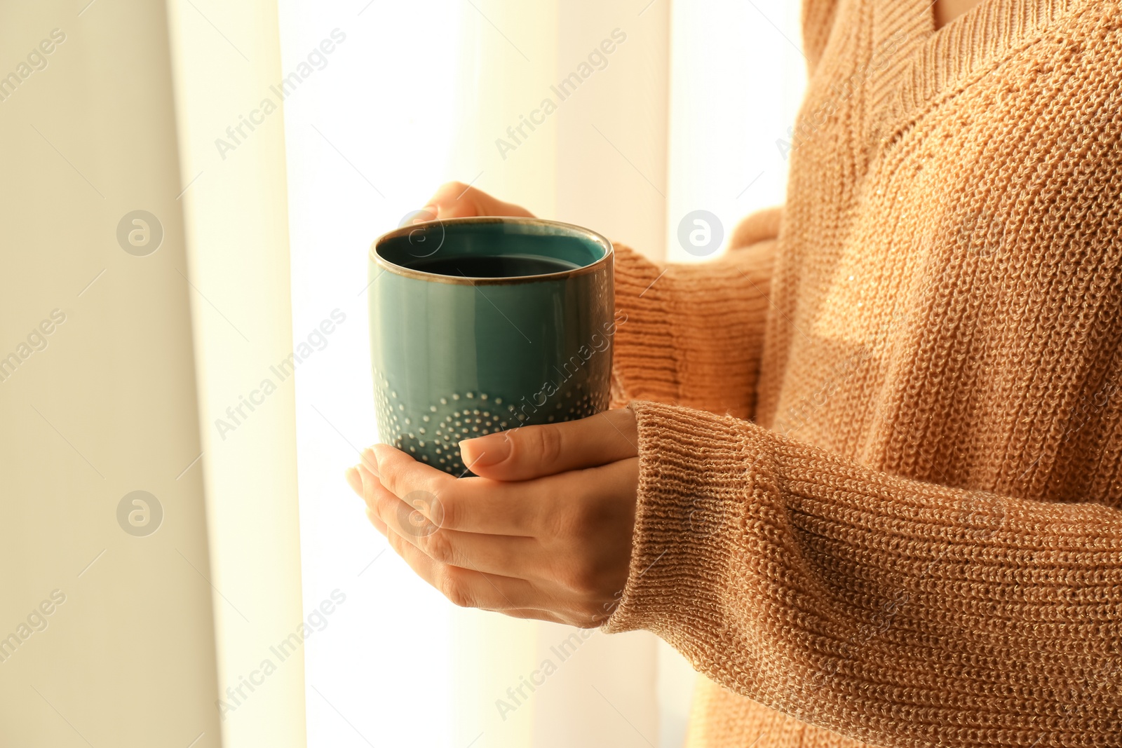 Photo of Woman holding elegant cup with tea near window indoors, closeup