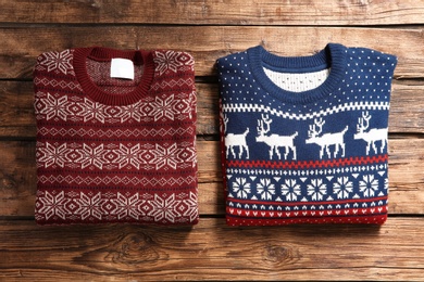 Photo of Christmas sweaters with pattern on wooden background, top view