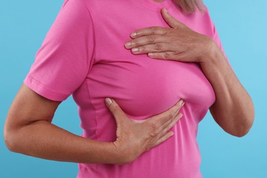 Photo of Woman doing breast self-examination on light blue background, closeup