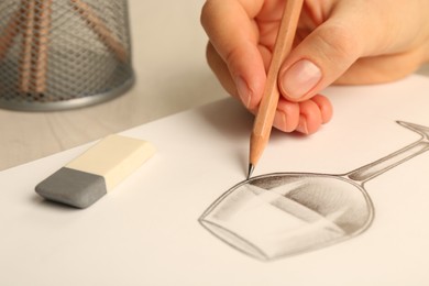 Woman drawing glass of wine with graphite pencil at light wooden table, closeup