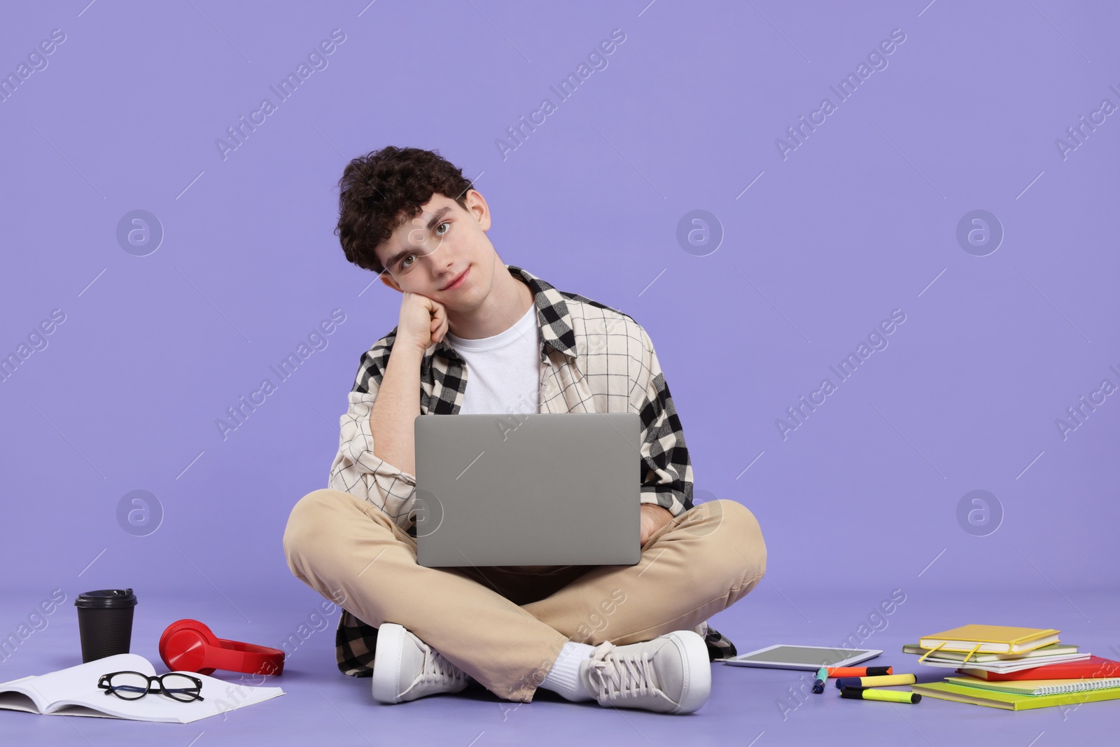 Photo of Portrait of student with laptop and stationery sitting on purple background