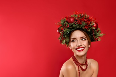 Beautiful young woman wearing Christmas wreath on red background. Space for text