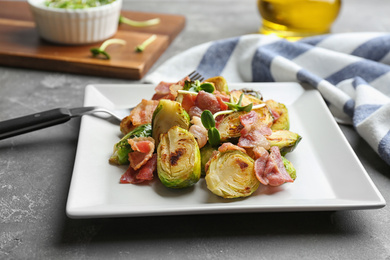 Photo of Delicious roasted Brussels sprouts with bacon served on grey table