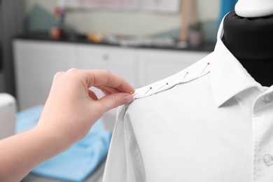 Seamstress putting pins into semi-ready shirt in tailor workshop, closeup