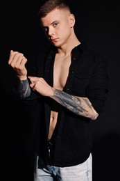 Photo of Young man with tattoos in black shirt on dark background