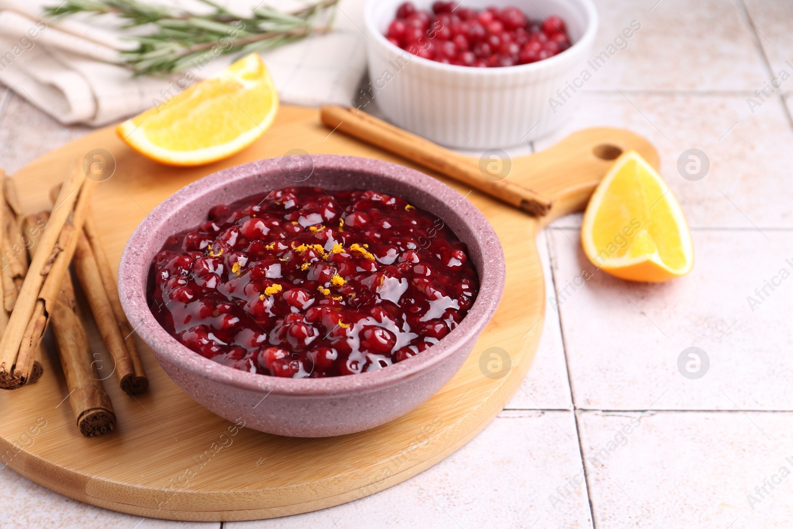 Photo of Tasty cranberry sauce in bowl and ingredients on white tiled table, space for text