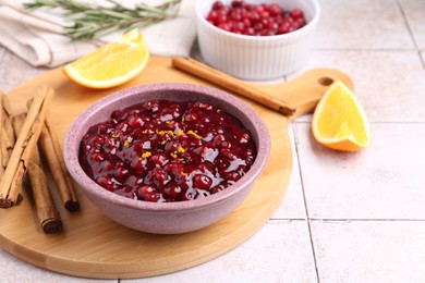 Tasty cranberry sauce in bowl and ingredients on white tiled table, space for text