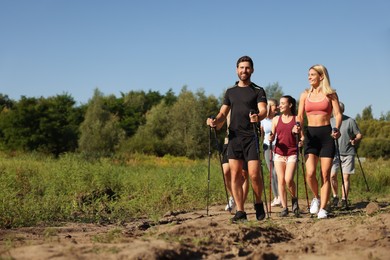 Photo of Group of happy people practicing Nordic walking with poles outdoors on sunny day