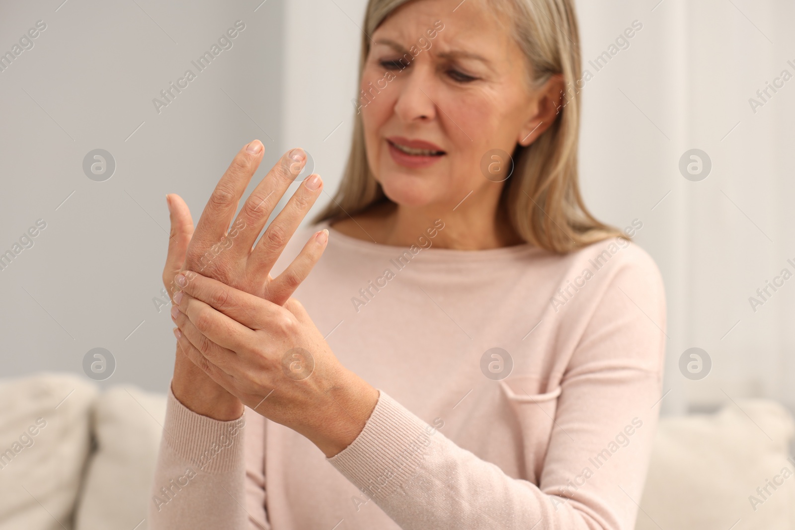 Photo of Mature woman suffering from pain in hand indoors, selective focus. Rheumatism symptom