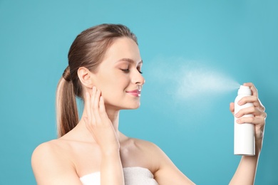 Young woman applying thermal water on face against color background. Cosmetic product