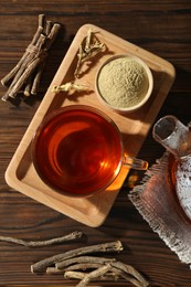 Photo of Aromatic licorice tea in cup, dried sticks of licorice root and powder on wooden table, flat lay