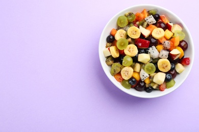 Delicious exotic fruit salad on purple background, top view. Space for text