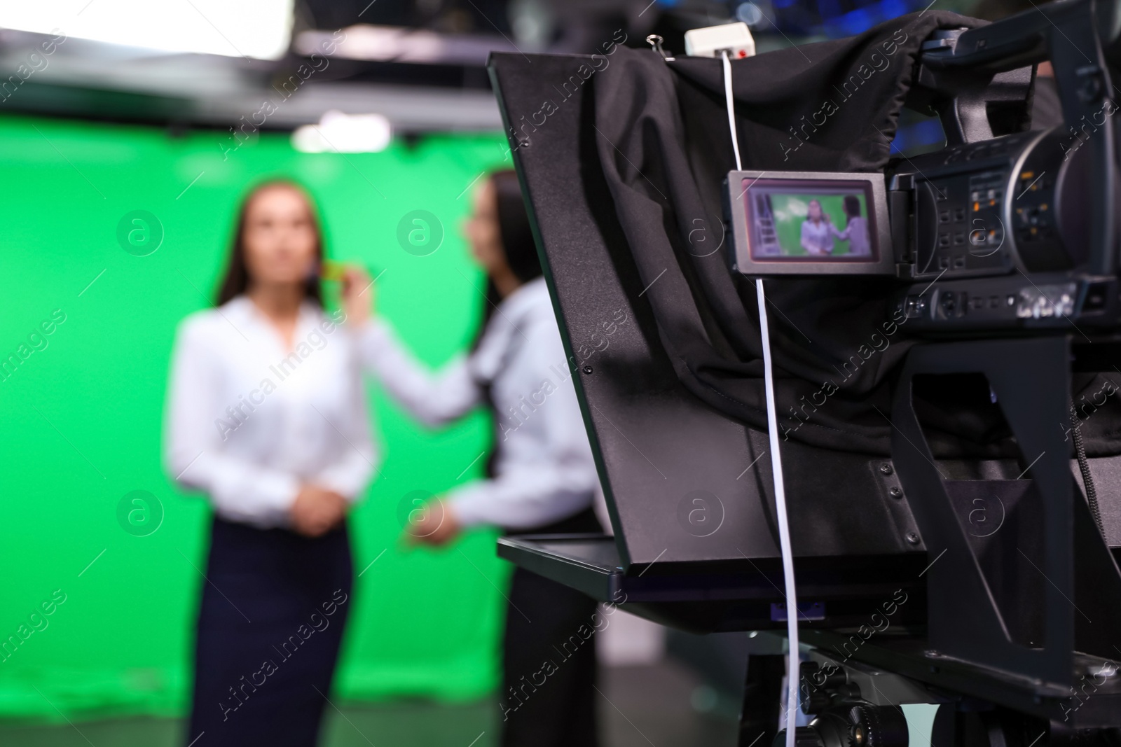 Photo of Presenter and makeup artist working in studio, focus on video camera