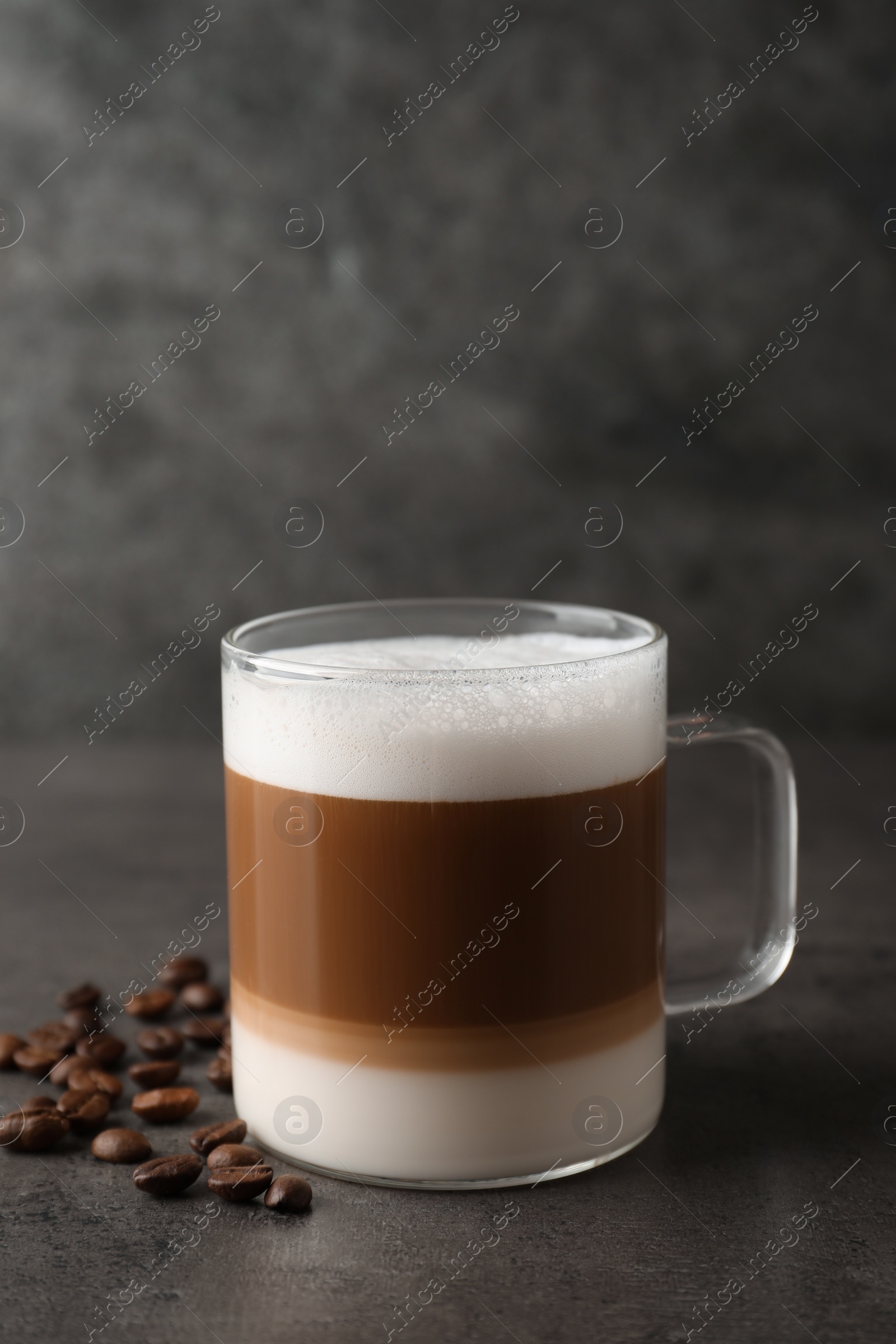 Photo of Hot coffee with milk in glass cup and beans on grey table