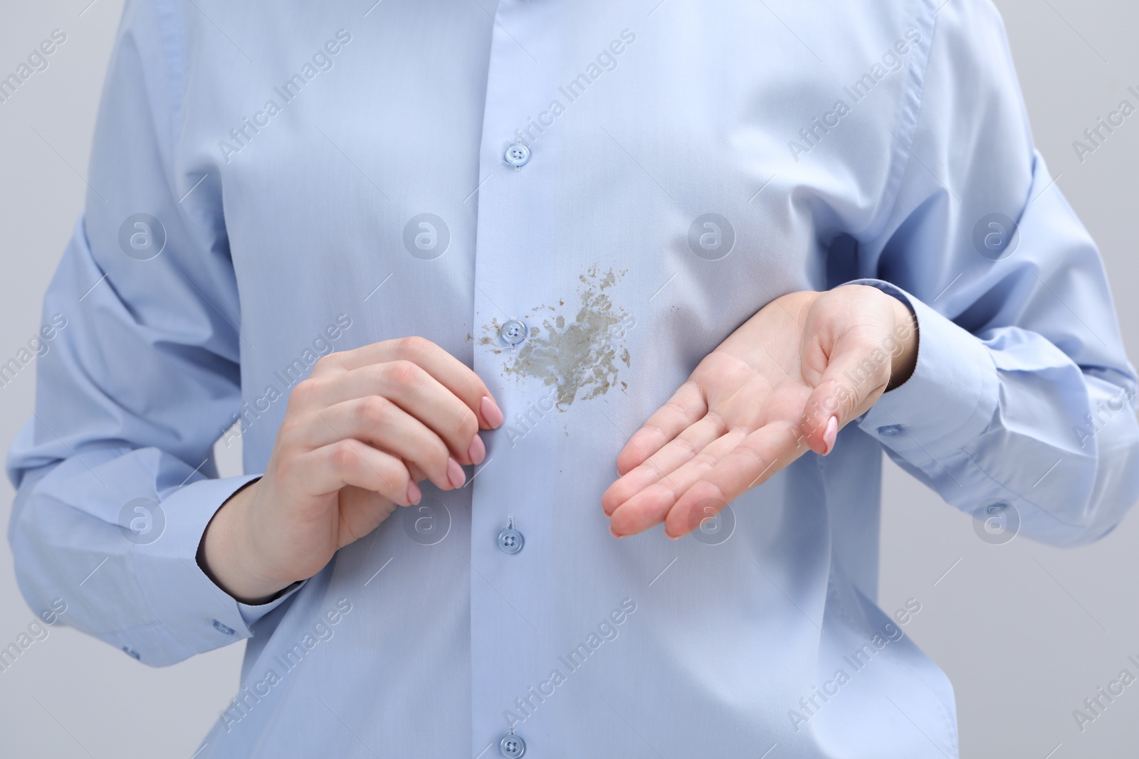 Photo of Woman showing stain on her shirt against light grey background, closeup