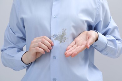 Photo of Woman showing stain on her shirt against light grey background, closeup