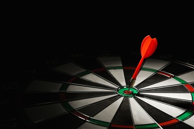 Photo of Red arrow hitting target on dart board against black background. Space for text