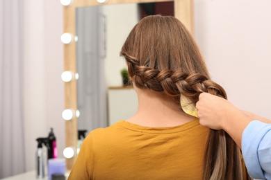 Professional coiffeuse braiding client's hair in salon