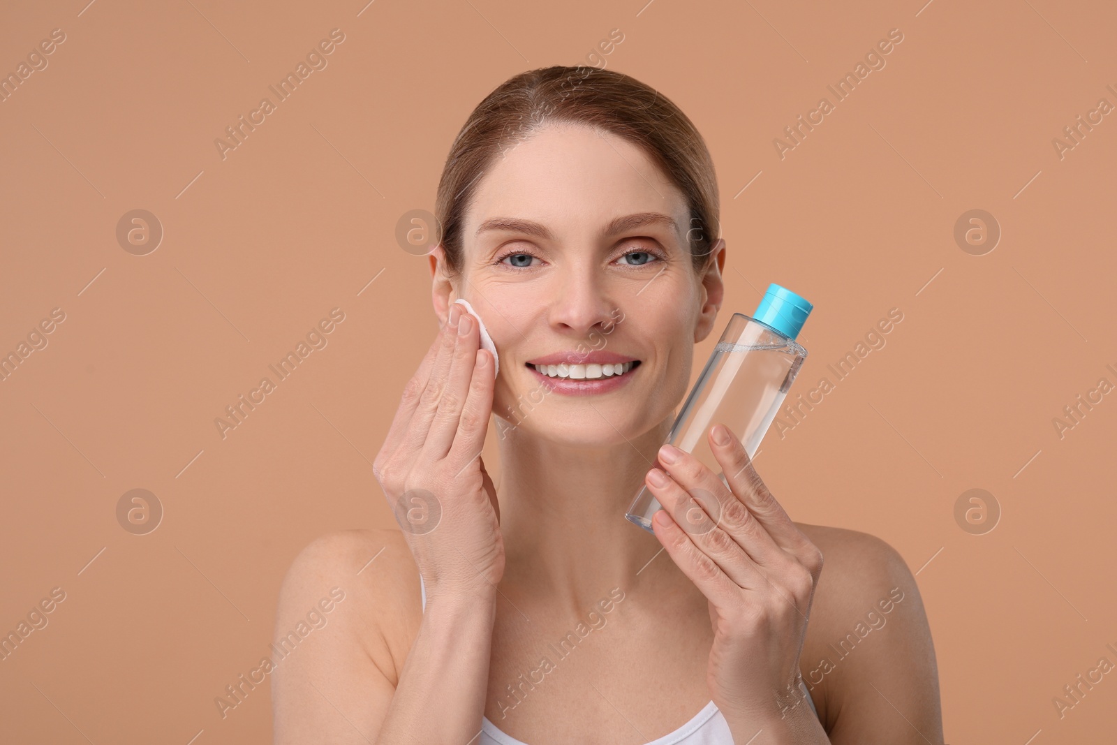 Photo of Beautiful woman removing makeup with cotton pad on beige background