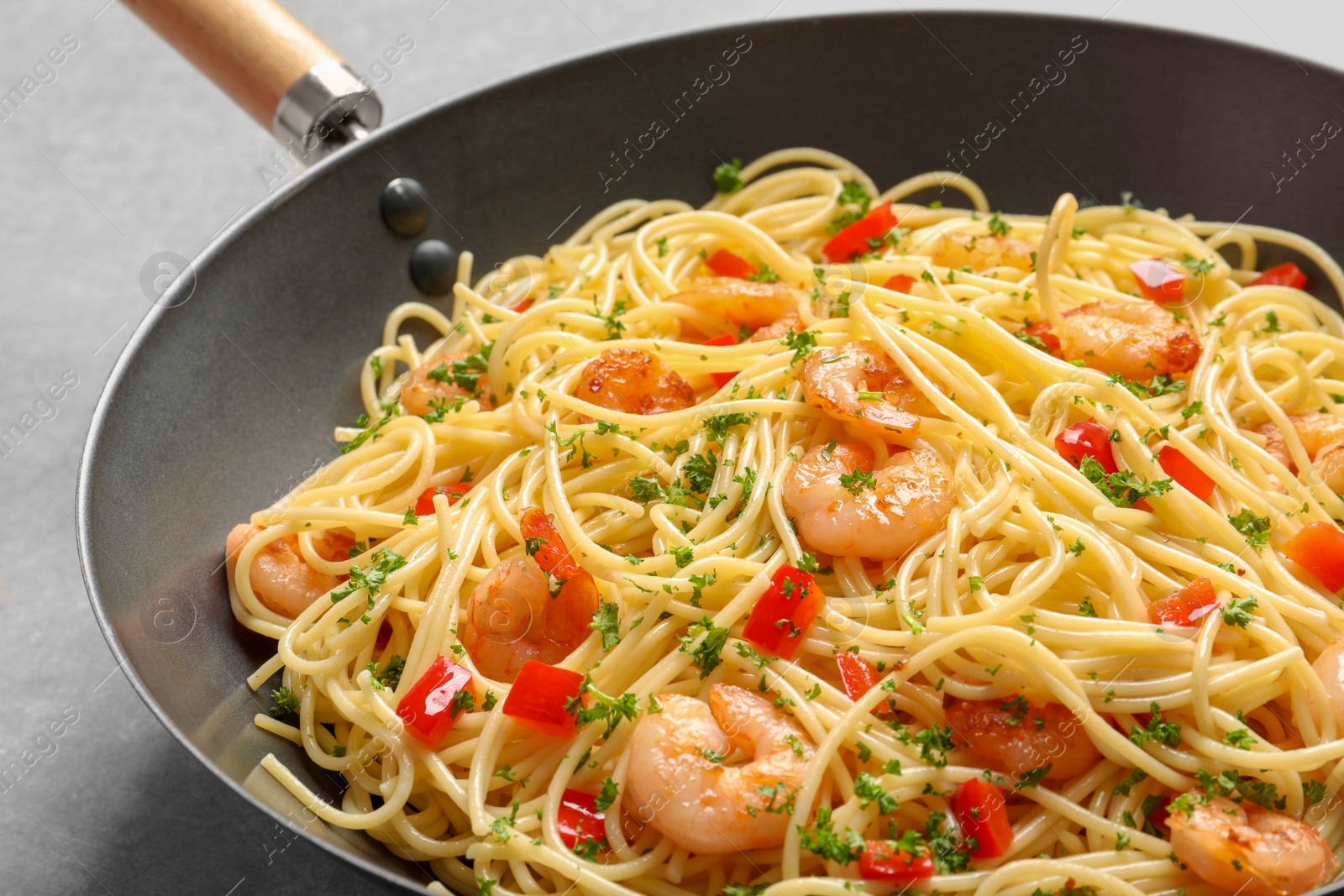 Photo of Frying pan with spaghetti and shrimps on light background, closeup