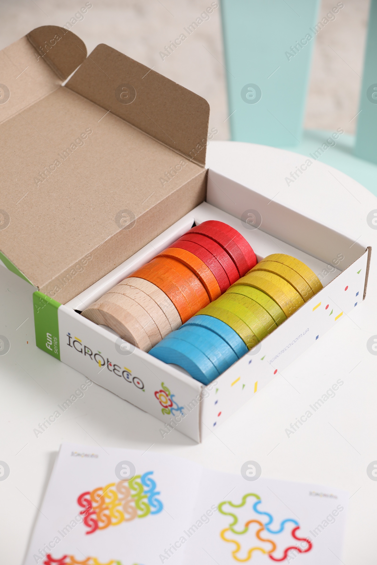 Photo of Box with colorful wooden pieces of playing set and cards on white table. Educational toy for motor skills development