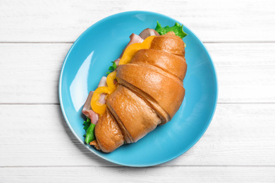 Tasty croissant sandwich with ham on white wooden table, top view