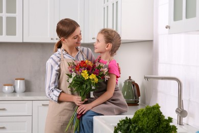 Photo of Little daughter congratulating mom with bouquet of flowers in kitchen. Happy Mother's Day