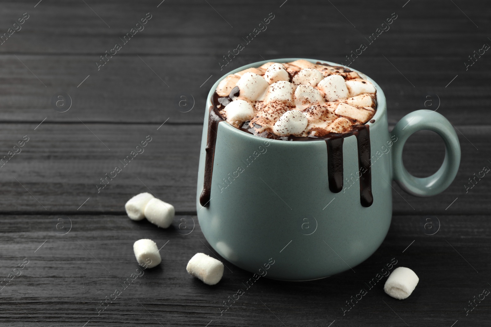 Photo of Cup of aromatic hot chocolate with marshmallows and cocoa powder on dark gray wooden table, closeup. Space for text