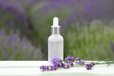 Bottle of essential oil and lavender flowers on white wooden table in field