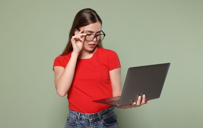 Photo of Beautiful woman in glasses with laptop on pale green background