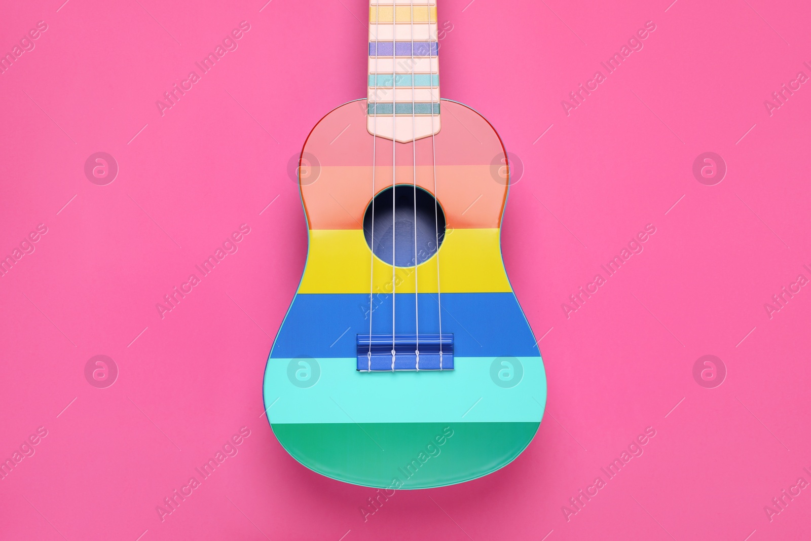 Photo of Colorful ukulele on pink background, top view. String musical instrument