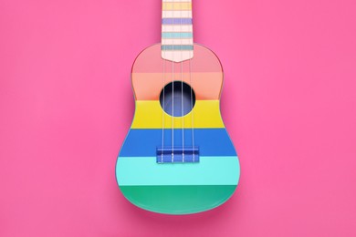 Colorful ukulele on pink background, top view. String musical instrument