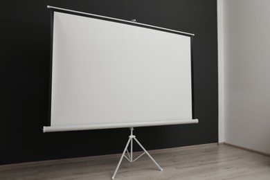 Photo of Blank projection screen near black wall indoors. Space for design