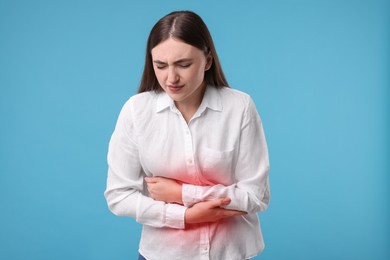 Woman suffering from abdominal pain on light blue background
