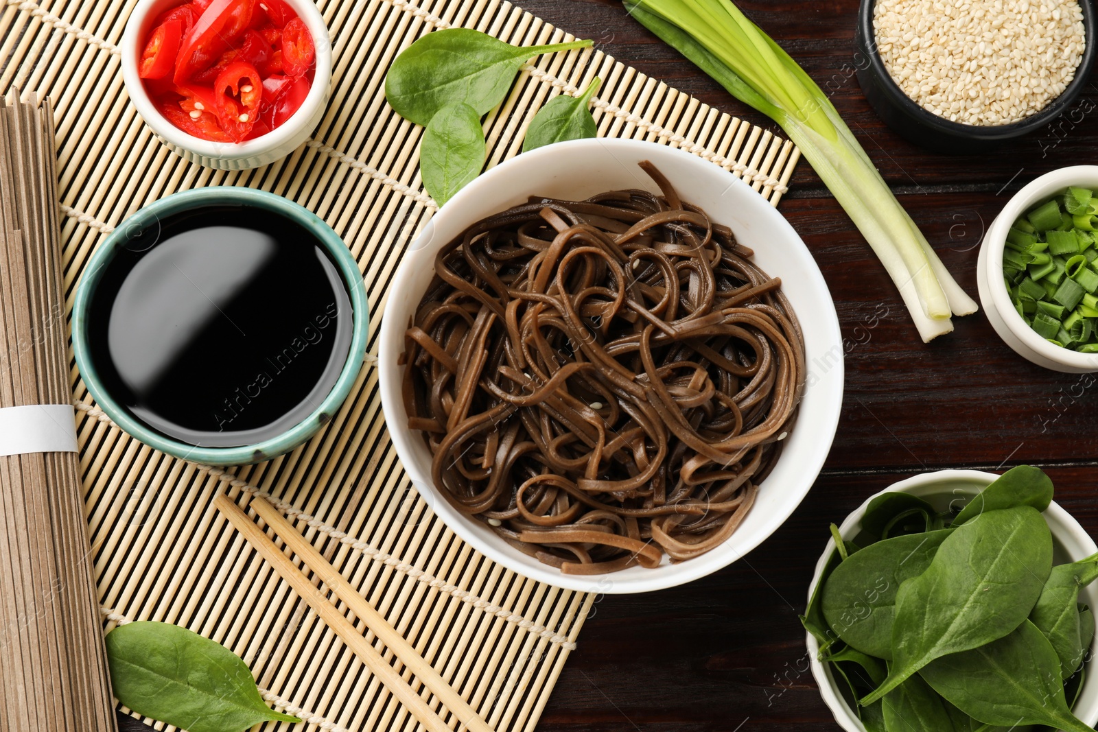 Photo of Tasty buckwheat noodles (soba) with ingredients and chopsticks on wooden table, flat lay