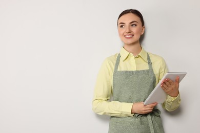 Photo of Beautiful young woman in clean apron with tablet on light grey background. Space for text