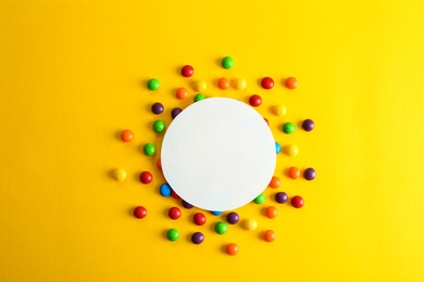 Colorful glazed candies and blank card on yellow background, flat lay. Space for text