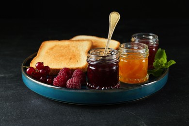 Plate with different jams, fresh berries and toasts on black table
