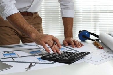 Architect working with construction drawings and calculator in office, closeup