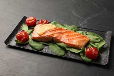 Tasty grilled salmon with tomatoes, spinach and lemon on black table