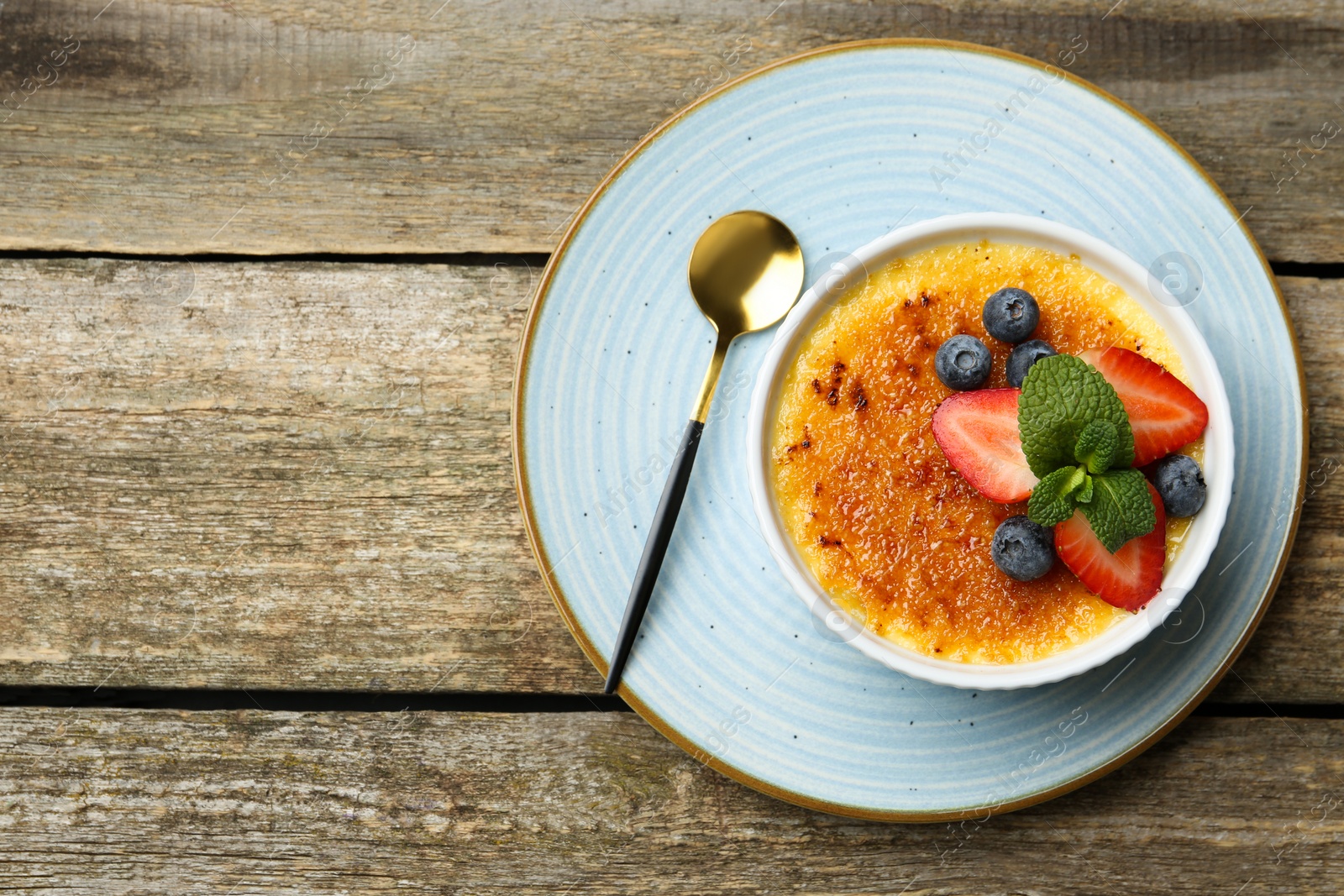 Photo of Delicious creme brulee with berries and mint in bowl on wooden table, top view. Space for text