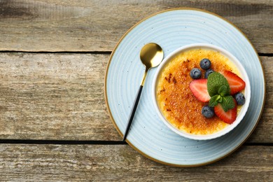 Photo of Delicious creme brulee with berries and mint in bowl on wooden table, top view. Space for text
