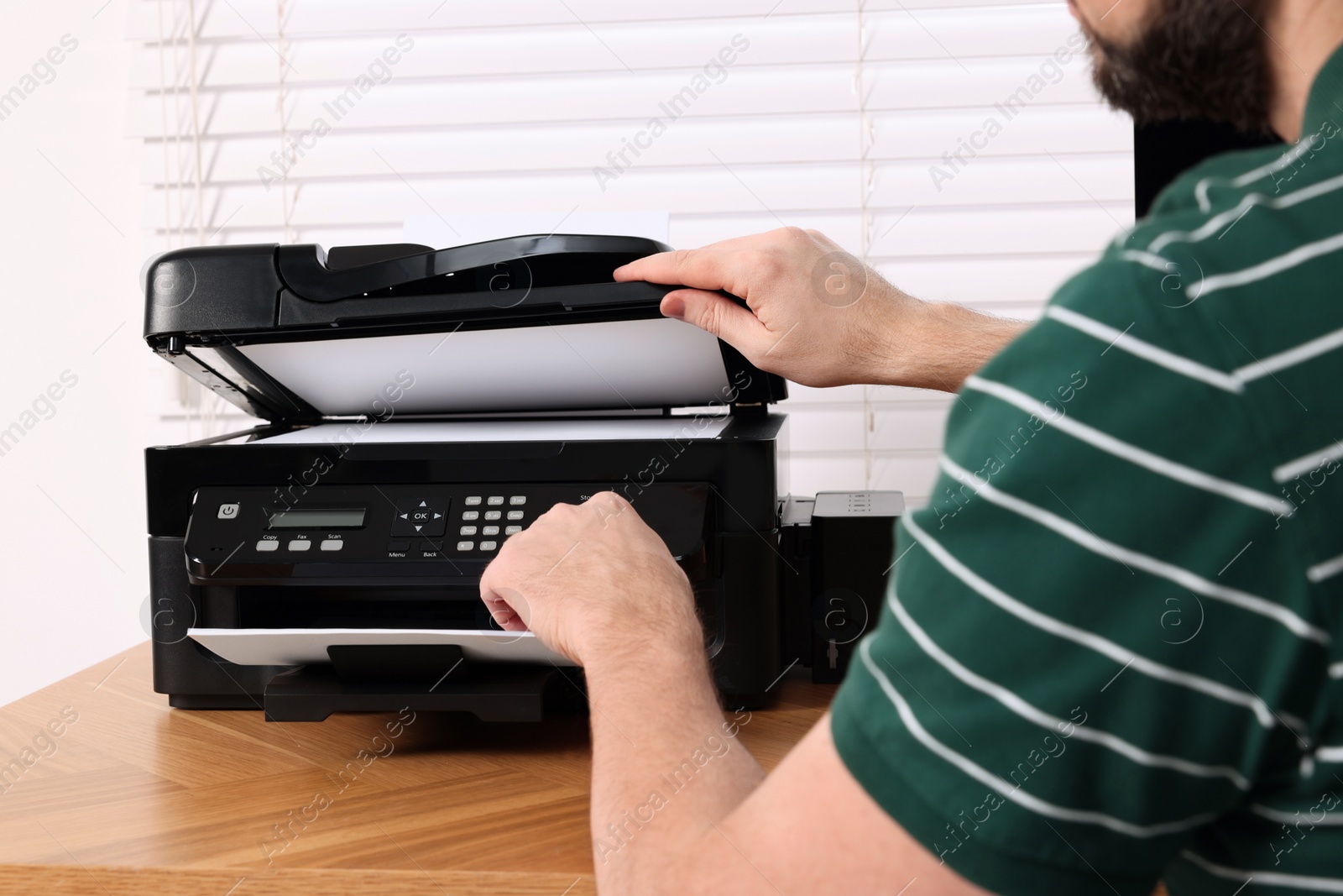 Photo of Man using modern printer at wooden table indoors, closeup