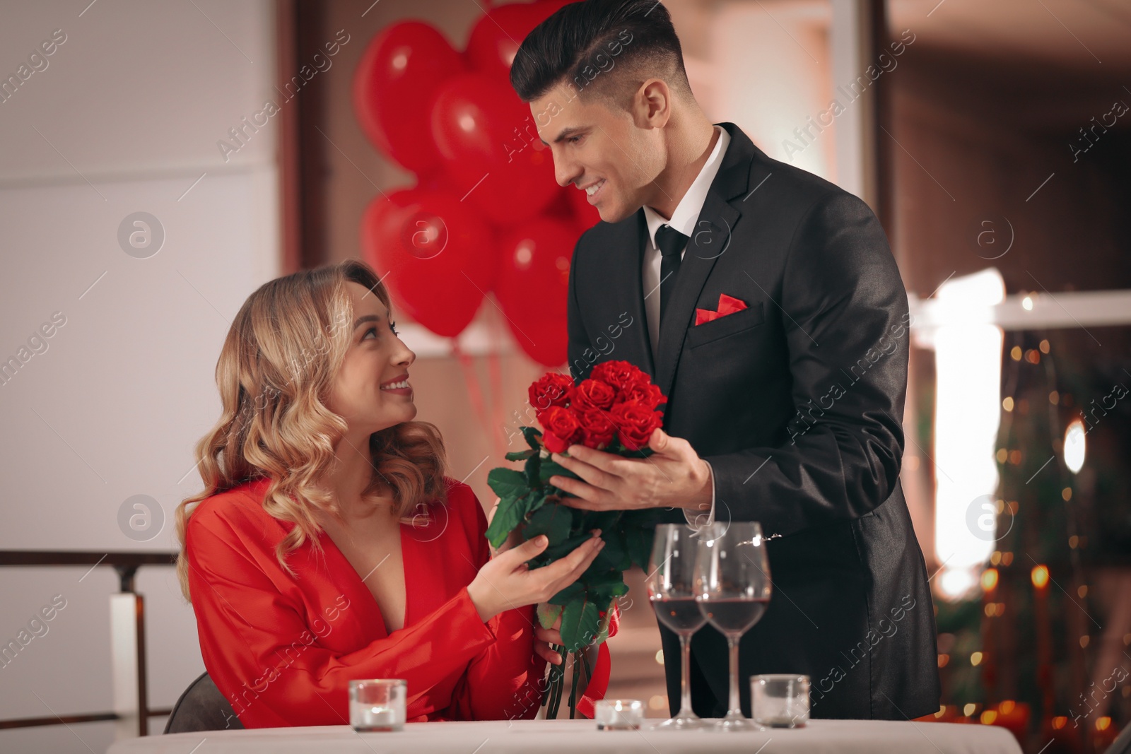 Photo of Man presenting roses to his beloved woman in restaurant at Valentine's day dinner