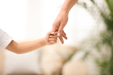 Photo of Mother holding hands with her child indoors, closeup. Happy family