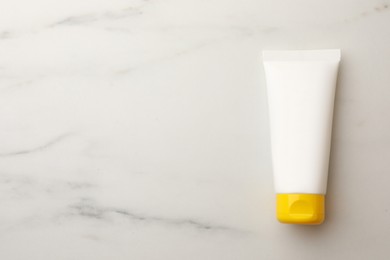 Photo of Face cream in tube on white marble table, top view. Space for text