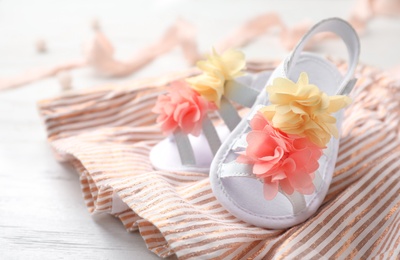 Photo of Pair of cute baby sandals and clothes on table