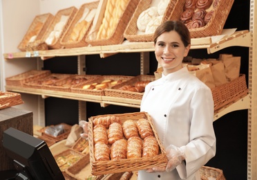 Professional baker holding tray with fresh buns in store