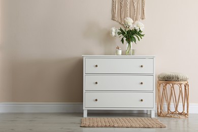 Room interior with white chest of drawers near beige wall. Space for text